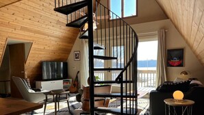 A loft-style room with a spiral staircase, a wooden ceiling, a sofa, a dining table, and a guitar. - Pepin’s Premier Waterfront Stay — The Dockside (Pepin)