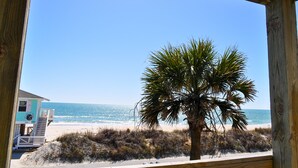 A beach view from a wooden structure with a palm tree in the foreground. - Sandy By The Sea | Gorgeous Oceanfront Retreat + Private Elevator! (North Topsail Beach)