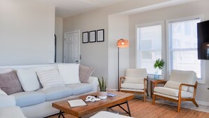 A living room with a sofa, two armchairs, a coffee table, and a floor lamp. - Sandy By The Sea | Gorgeous Oceanfront Retreat + Private Elevator! (North Topsail Beach)