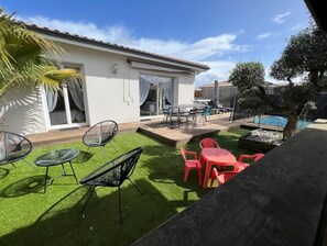 Enjoy outdoor dining and relaxation on the patio with a dining set and chairs, surrounded by a swimming pool and lush lawn.