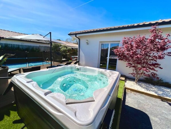 Relax in a hot tub adjacent to a shared pool, surrounded by a landscaped garden.