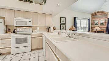 A modern kitchen with white appliances, wooden cabinets, a large sink, and a window with curtains.