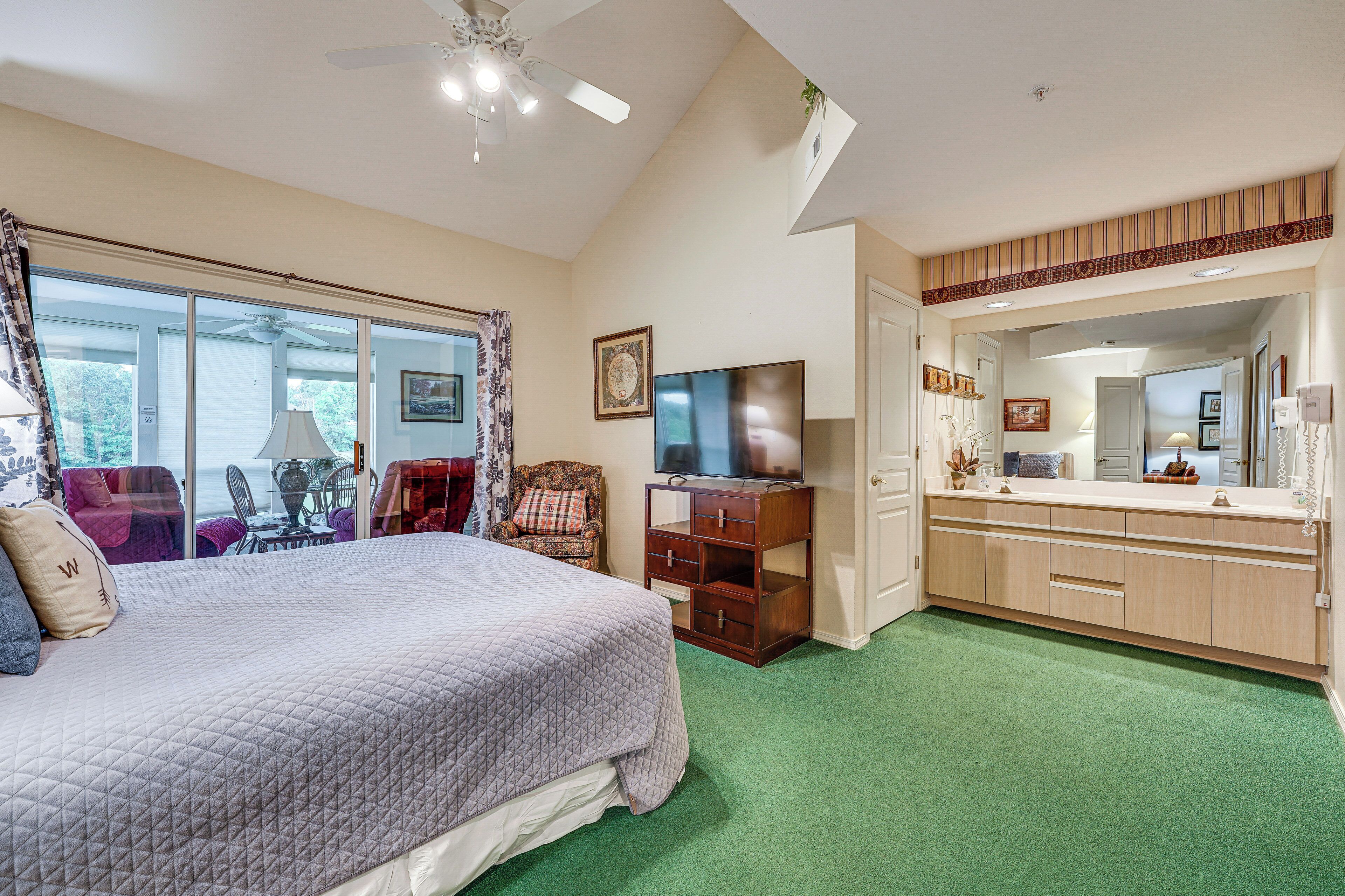 A bedroom with a bed, a TV, a dresser, and a bathroom with a mirror and sink.