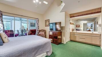 A bedroom with a bed, a TV, a dresser, and a bathroom with a mirror and sink.