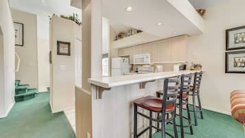 A modern kitchen with a bar area, green carpet, and a staircase leading to another level.
