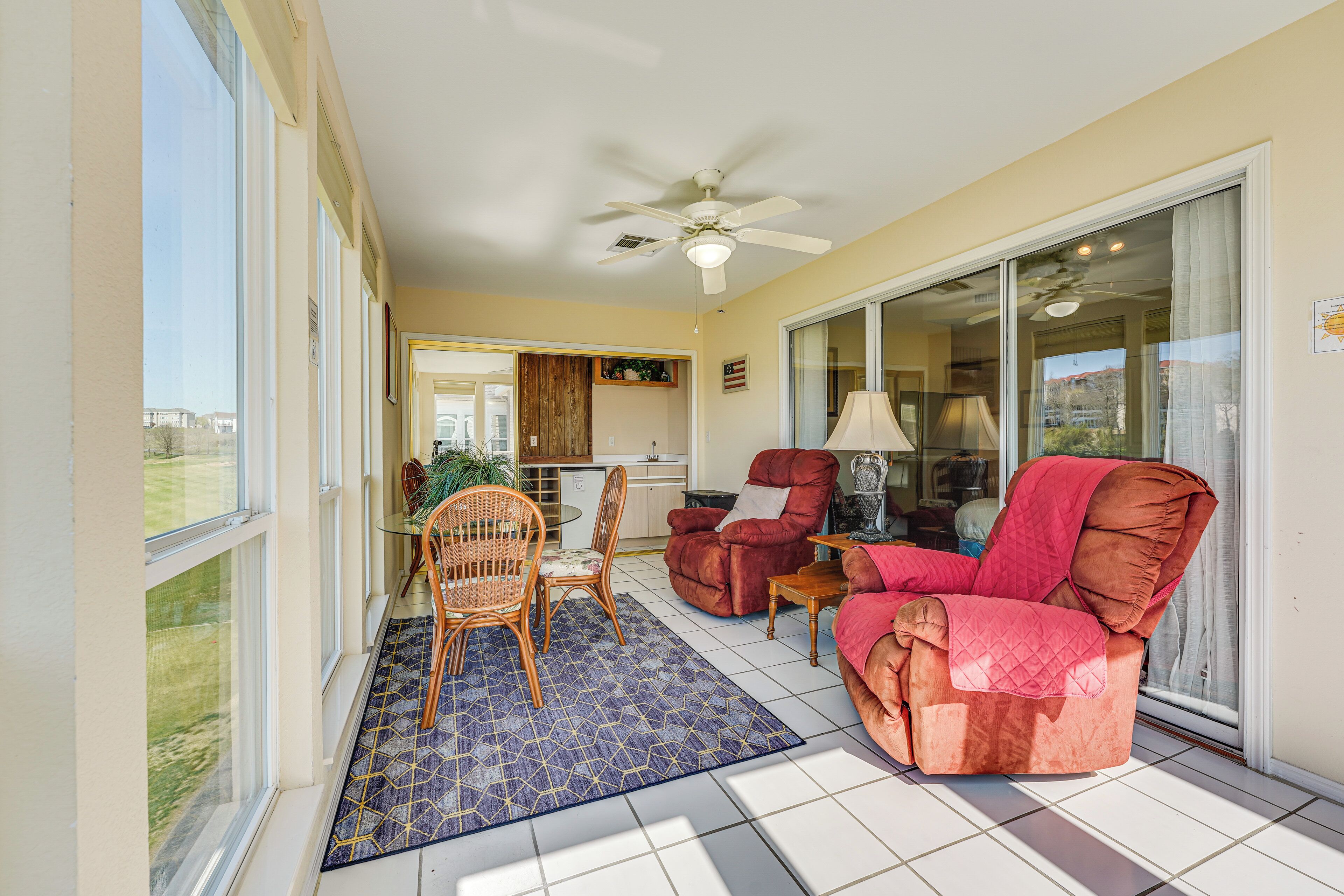 A spacious living area with a large sliding glass door leading to a balcony, a ceiling fan, and a dining table with chairs.