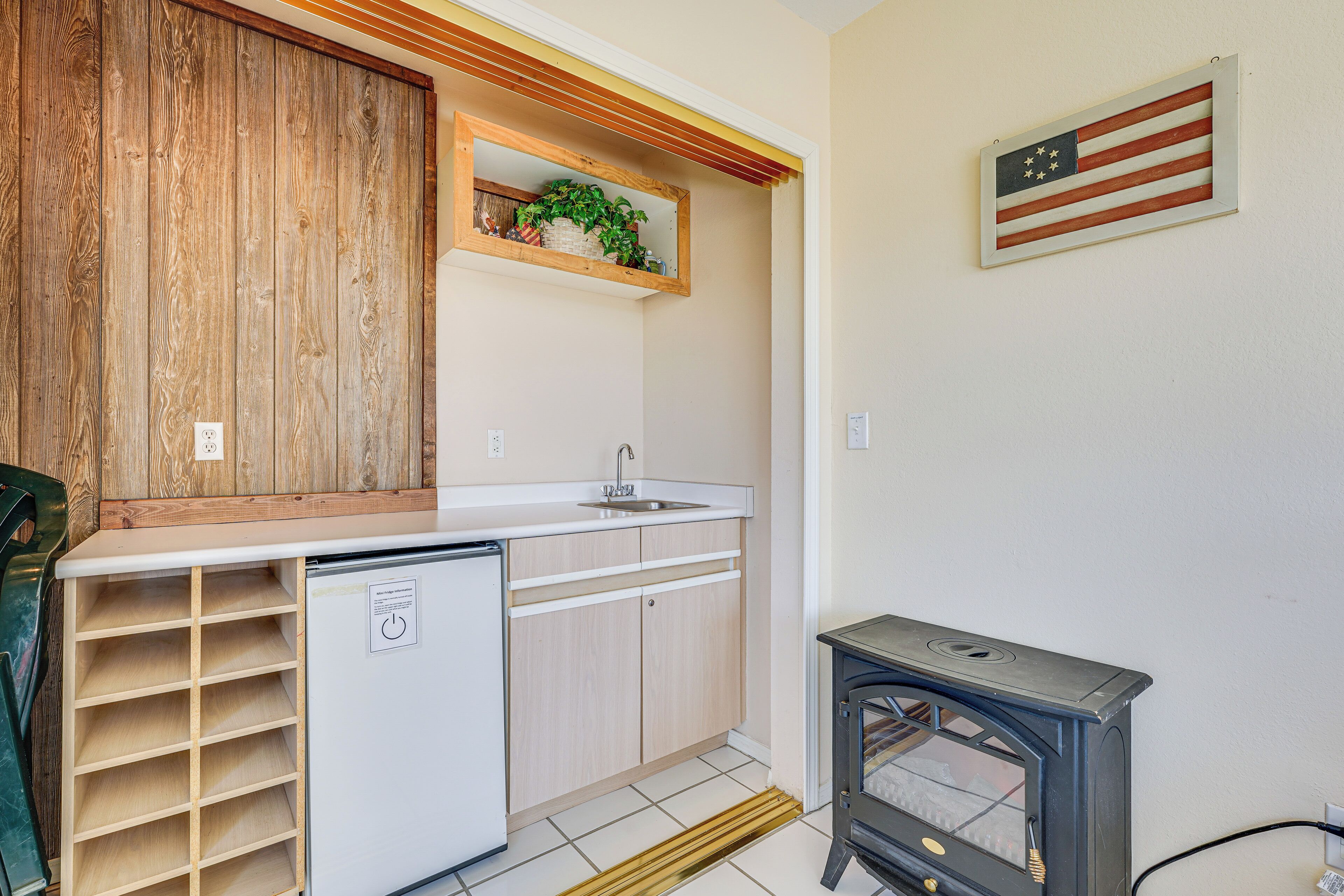 A compact kitchen with a built-in refrigerator, a sink, wooden cabinets, a small stove, and a wooden wall panel.