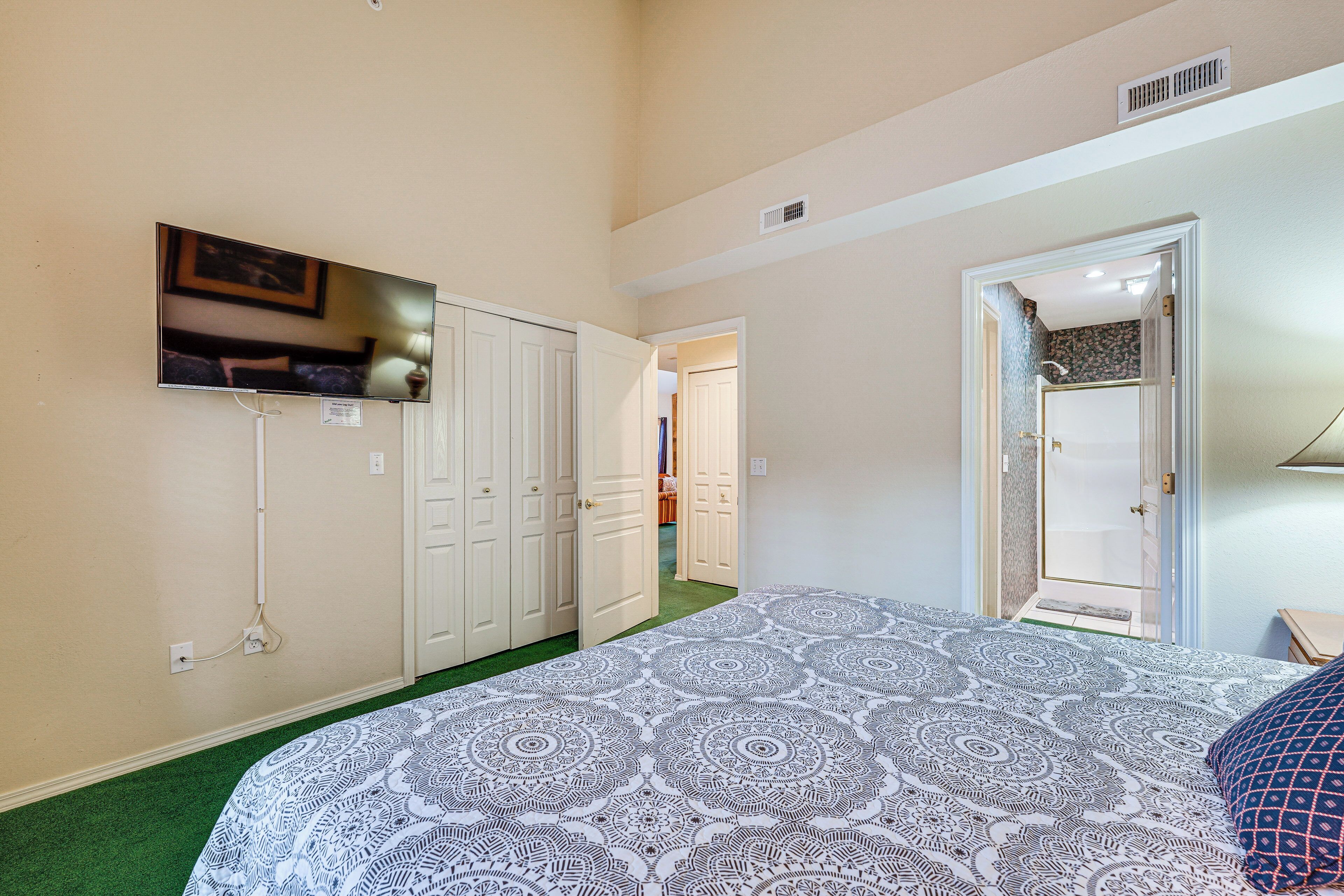 A bedroom with a patterned bedspread, a television mounted on the wall, and a door leading to another room.