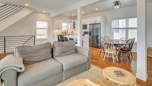 A spacious living area with a grey sofa, a dining table with chairs, and a kitchen in the background. - The Kraken Wildwood Townhome: 1/2 Mi to Beach! (Wildwood)