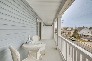 Ein Balkon mit weißen Korbmöbeln, einem kleinen Tisch und Blick auf eine Wohnstraße.