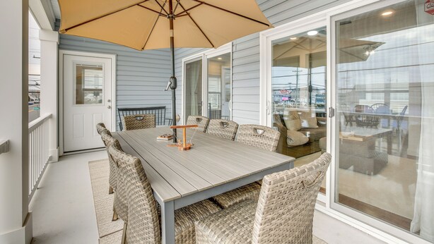 A dining area with a large table, wicker chairs, and a beige umbrella. - The Kraken Wildwood Townhome: 1/2 Mi to Beach! (Wildwood)