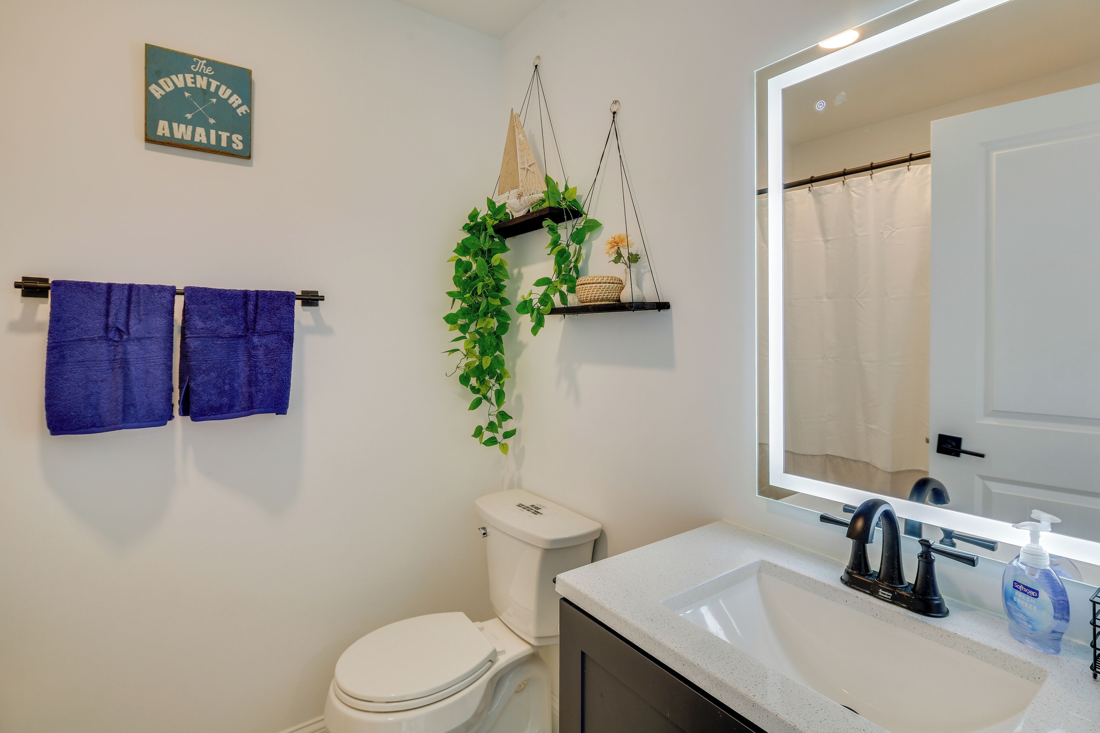 A bathroom with a white toilet, a sink with a mirror above it, and two blue towels hanging on a rack.