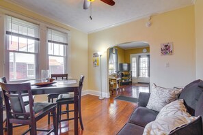 A dining area with a wooden table and chairs, a kitchen in the background, and a living room with a sofa and cushions. - Walk to Parks & Dining! Memphis Home w/ Yard (Memphis)
