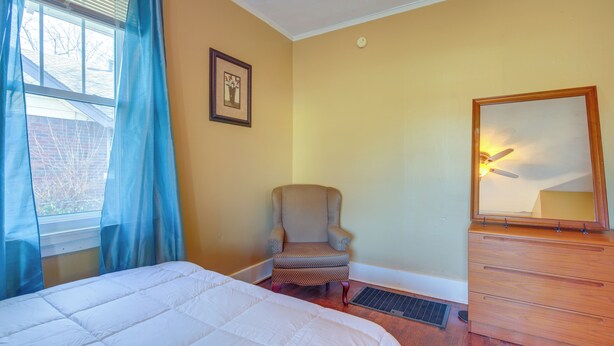 Une chambre à coucher avec un lit, une chaise, une commode et une fenêtre avec des rideaux.