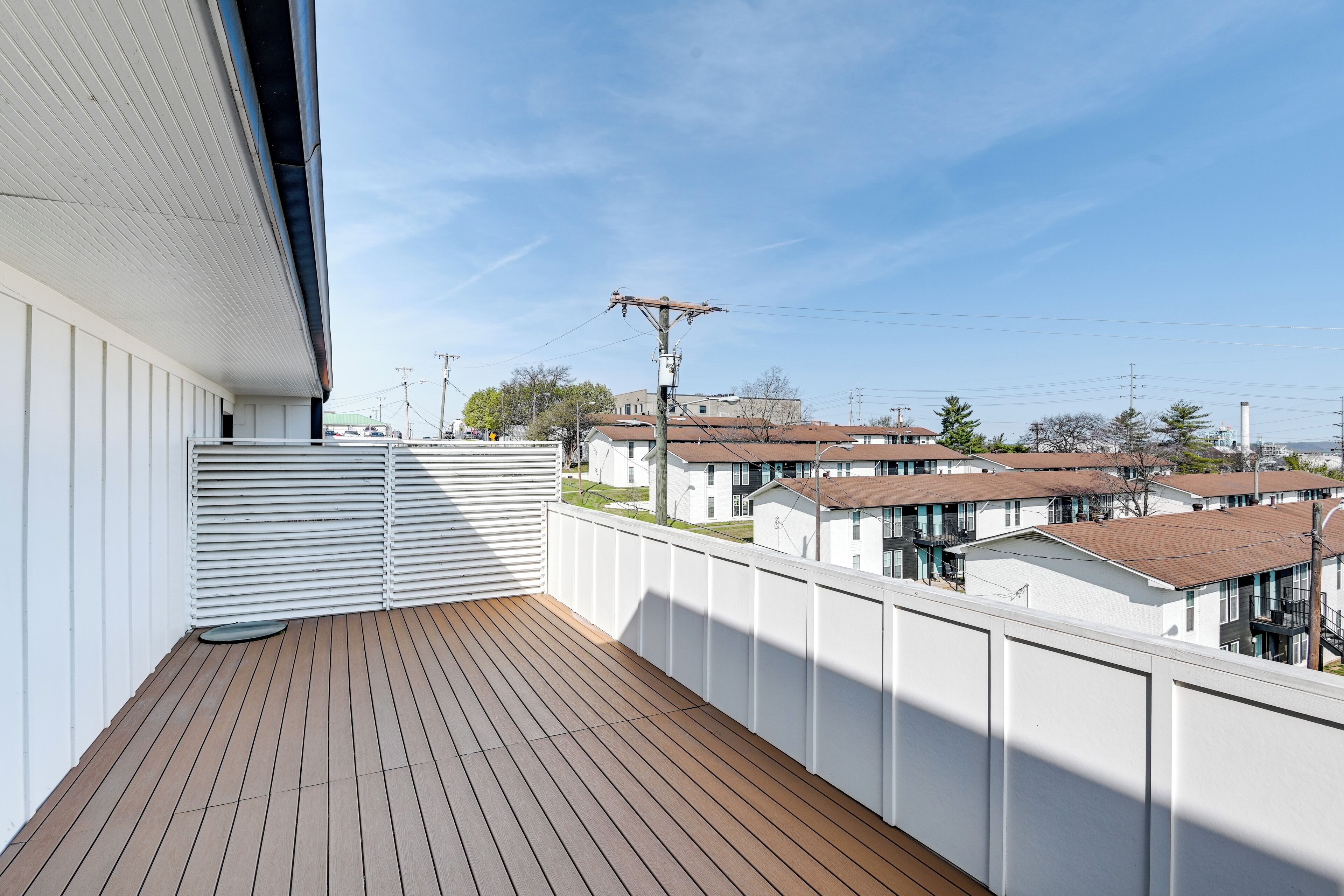 A balcony with a wooden floor, white railing, and a view of residential buildings in the background.