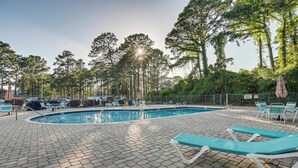 Une piscine entourée d’arbres et d’une clôture, avec des chaises longues et des parasols.