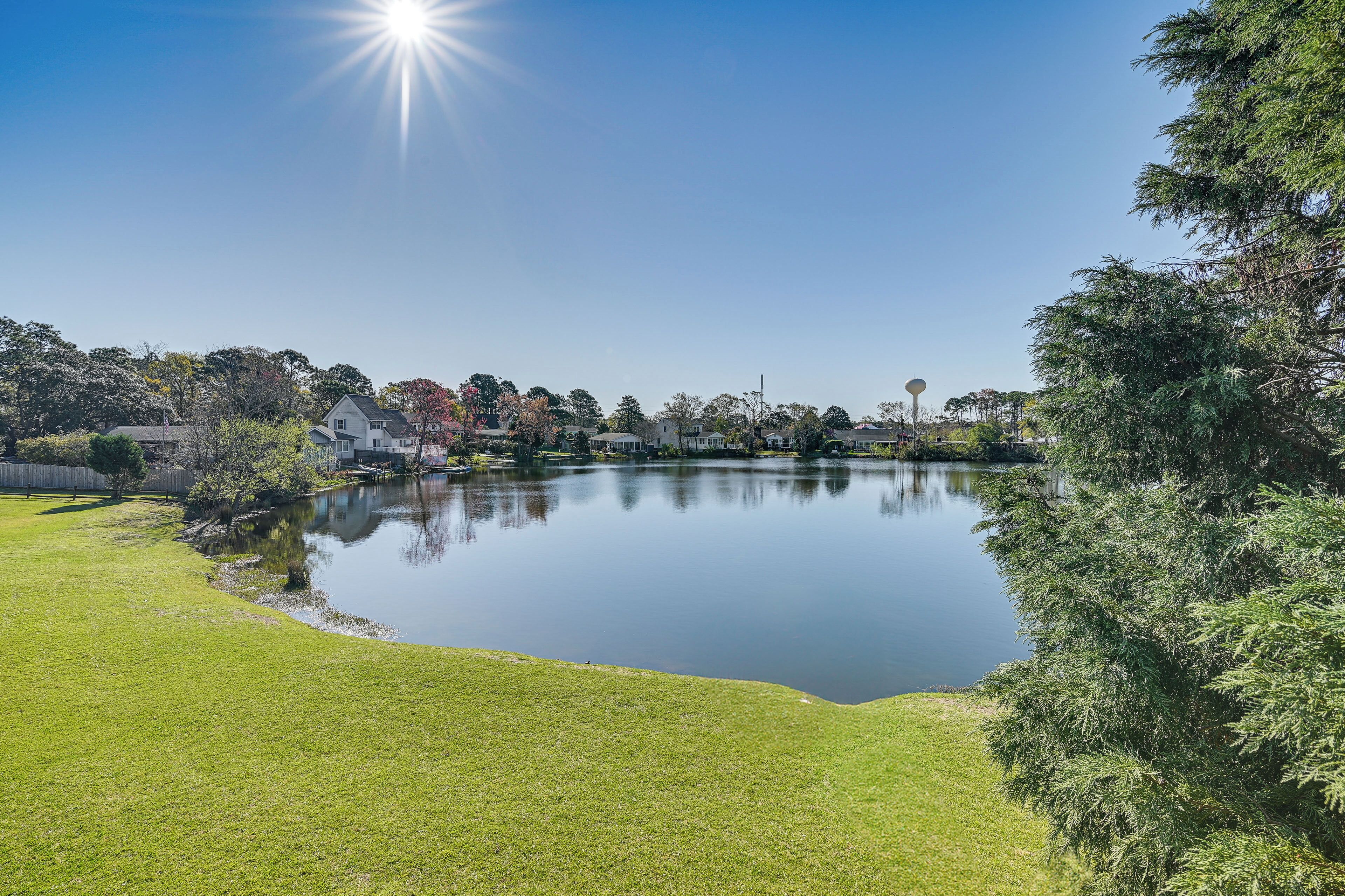 A serene lakeside view with a clear sky, calm water, and surrounding greenery.