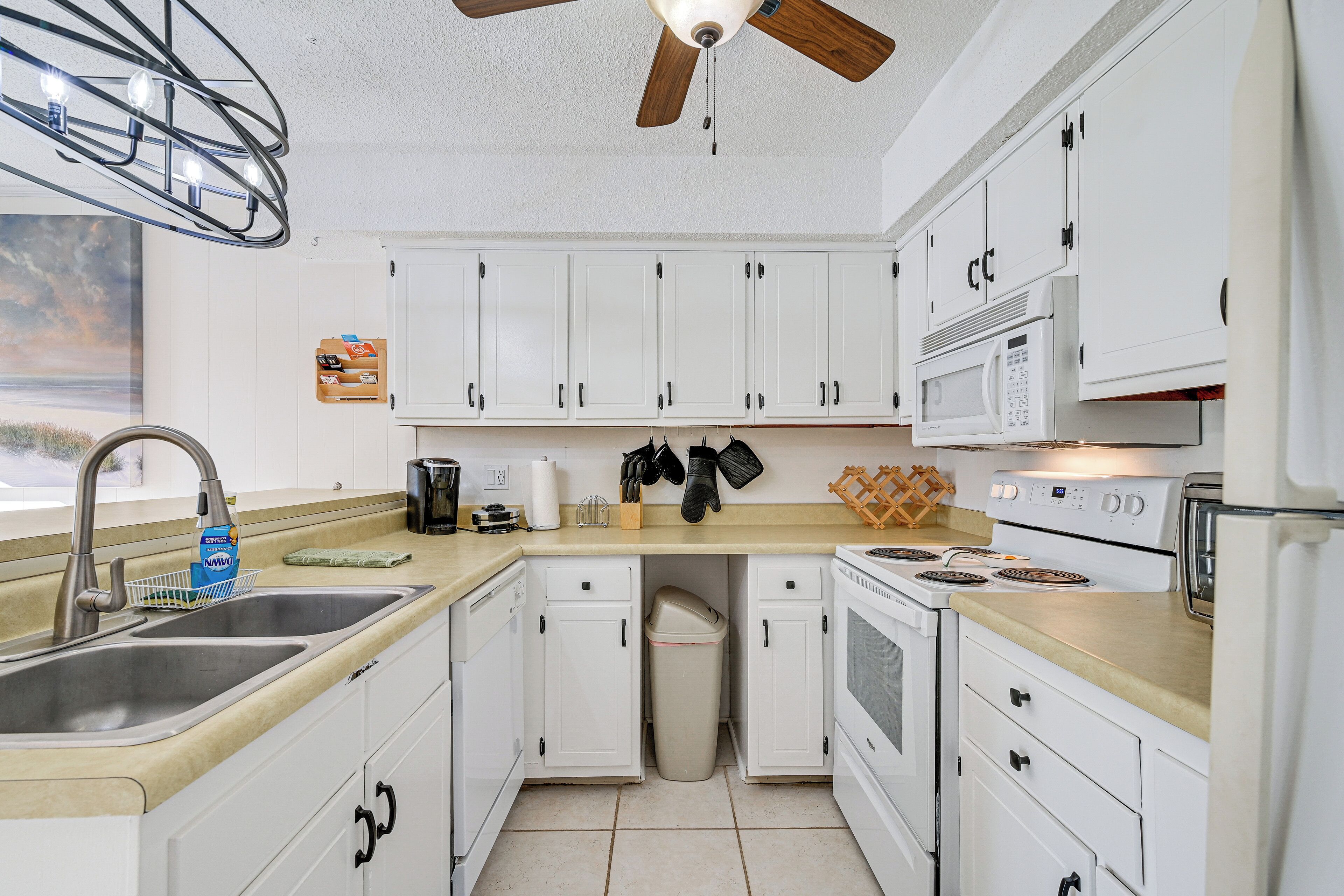 A modern kitchen with white cabinets, a stainless steel sink, a microwave, and a stove.