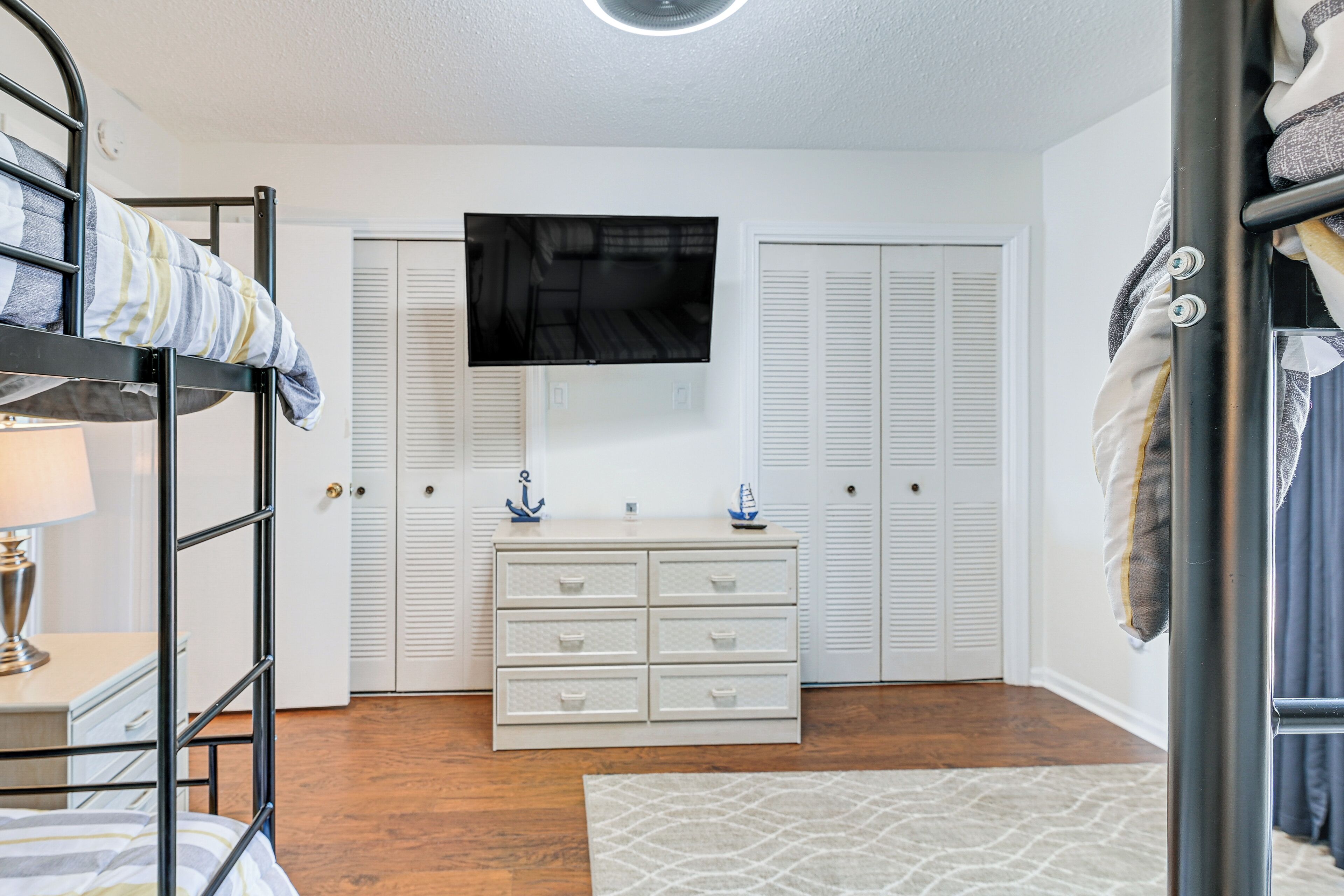 A bedroom with bunk beds, a dresser, a TV, and white closets.