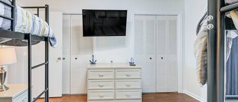 A bedroom with bunk beds, a dresser, a TV, and white closets.