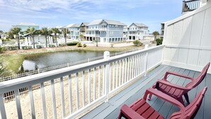 A balcony with a view of a lake, beach houses, and a white fence. - Island Cottage 1 Bedroom Townhouse by RedAwning (Navarre)