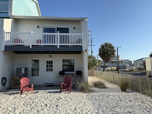 A two-story building with a balcony, a door, and a small outdoor seating area with chairs.