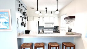 A kitchen with white cabinets, a microwave, and a sink. There are three wooden stools and a hanging light fixture. - Island Cottage 1 Bedroom Townhouse by RedAwning (Navarre)