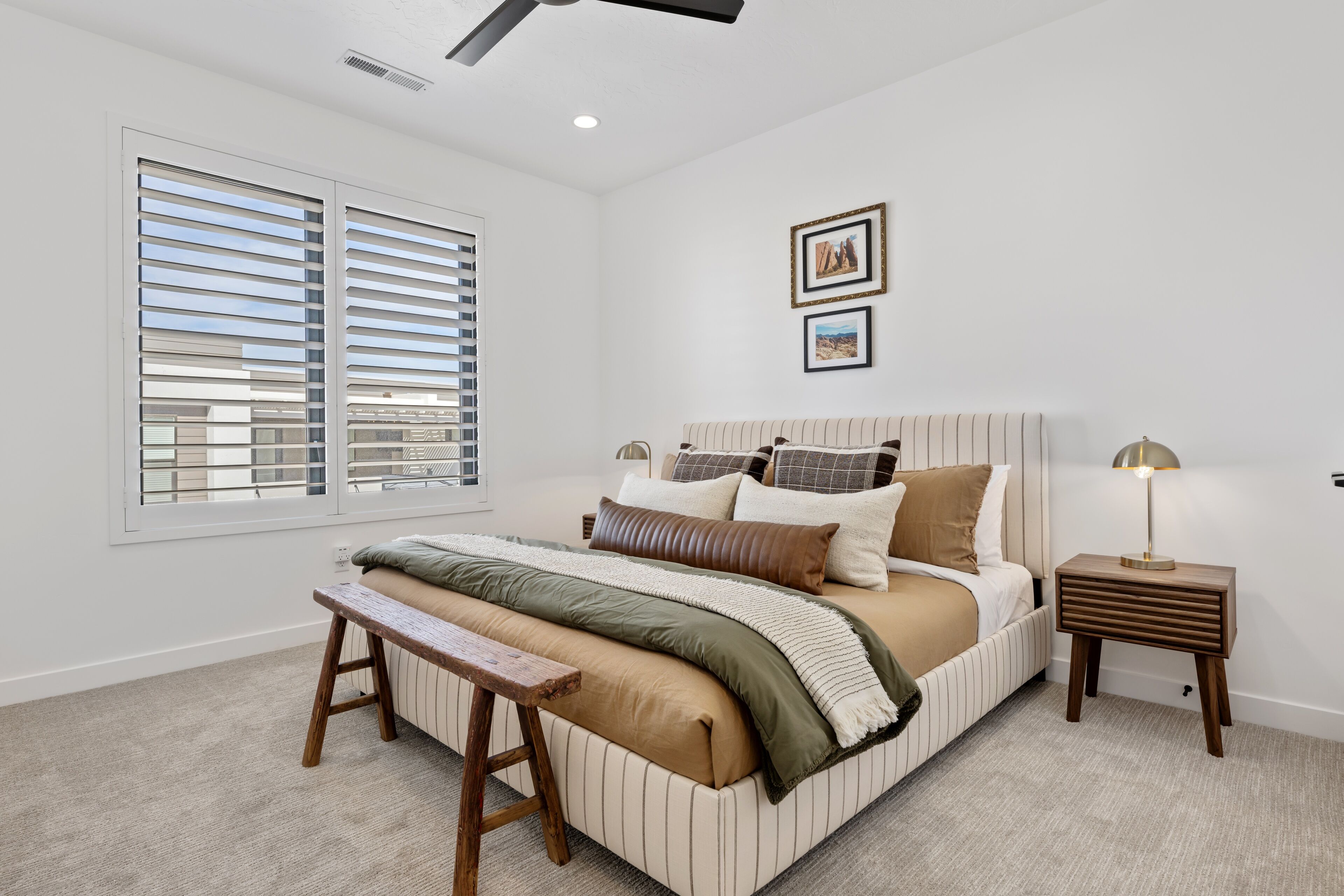 A bedroom with a large bed, a bench, a bedside table, and a window with blinds.