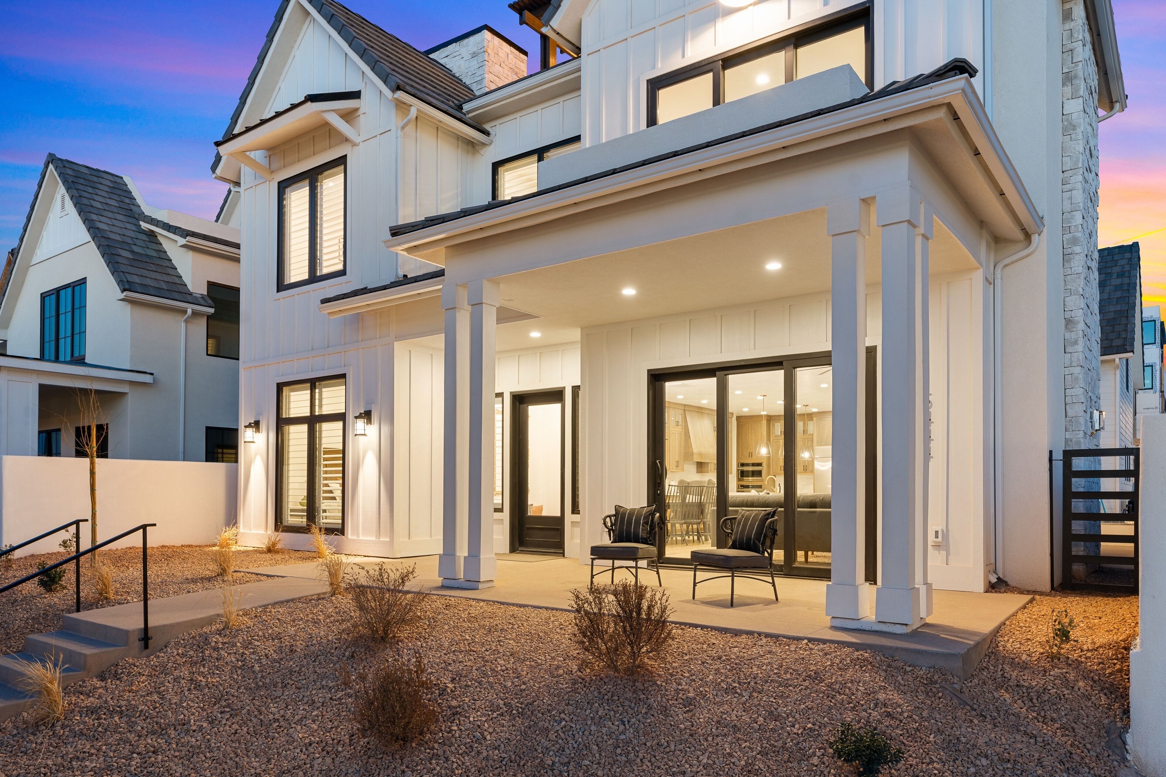A modern two-story house with a covered patio, large windows, and a well-lit entrance.