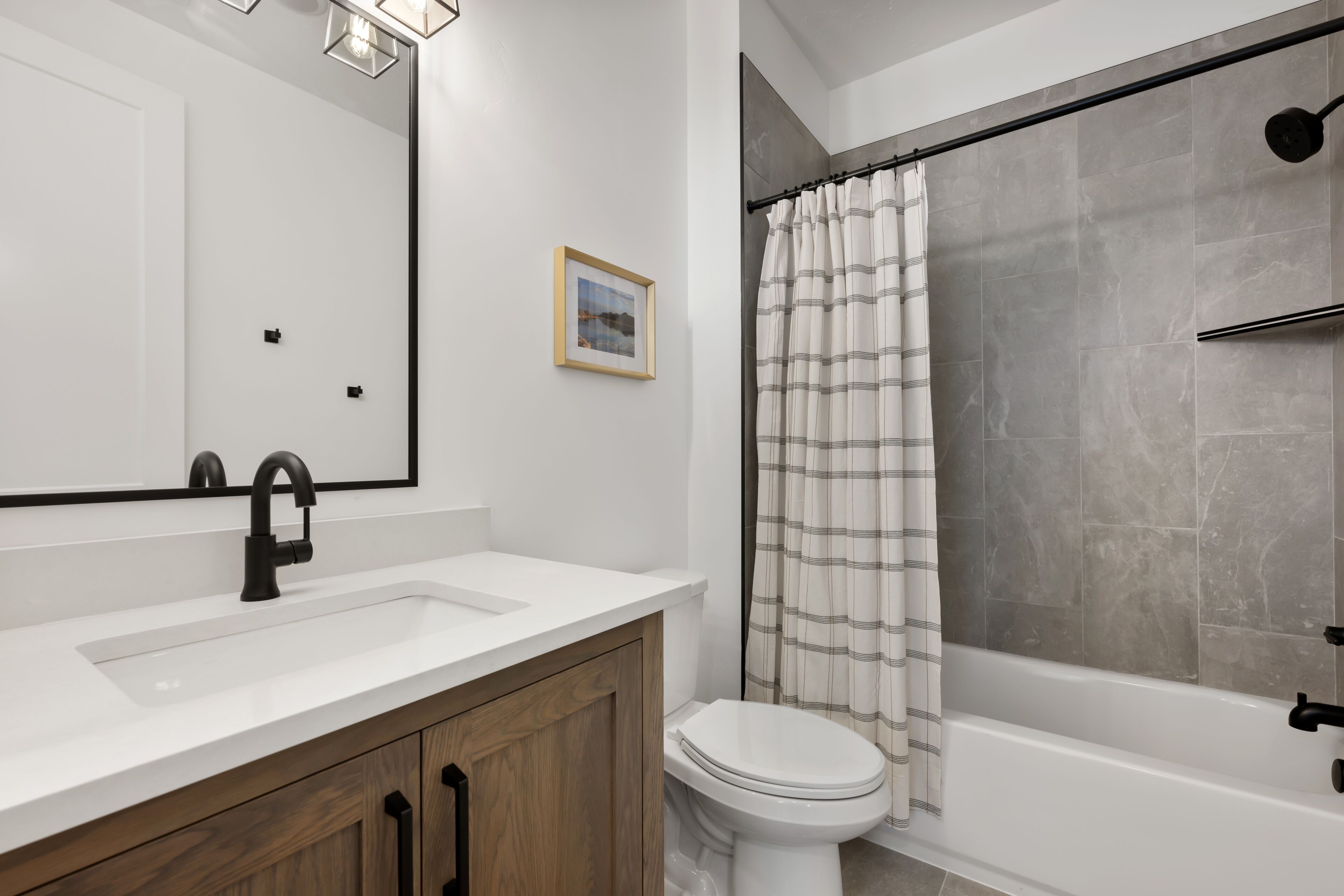 A modern bathroom with a white sink, wooden cabinets, a toilet, and a shower with a grey curtain.