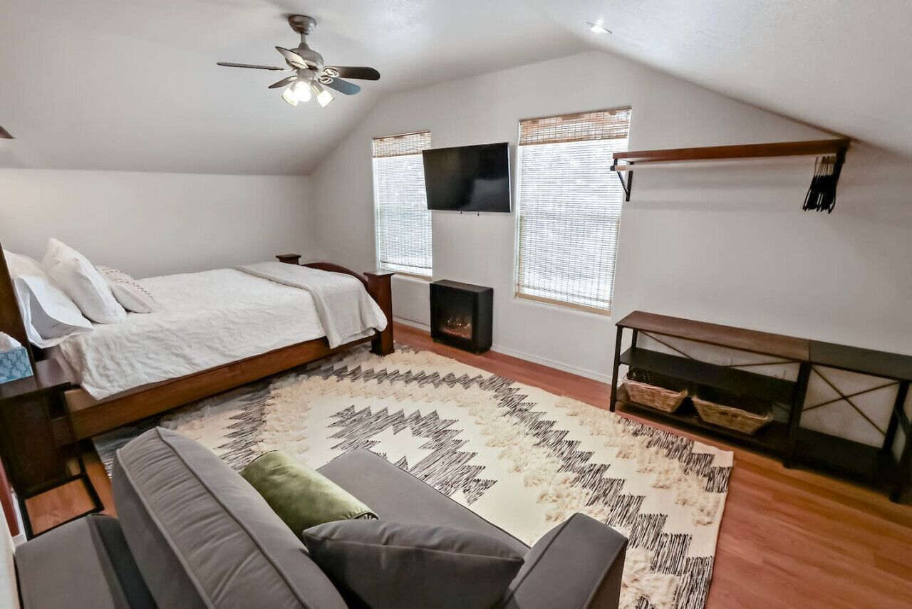 A bedroom with a bed, a sofa, a TV, and a ceiling fan.