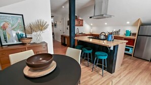Een moderne keuken met een centraal kookeiland, barkrukken en een eettafel met een schaal als decoratie.
