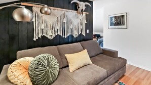 Een moderne woonkamer met een bruine bank, decoratieve kussens, een macramé wanddecoratie en een opgehangen schedel.