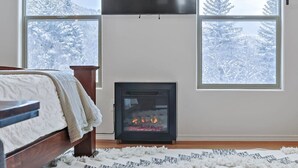 Een slaapkamer met een open haard, een bed en grote ramen met uitzicht op een besneeuwd bos.
