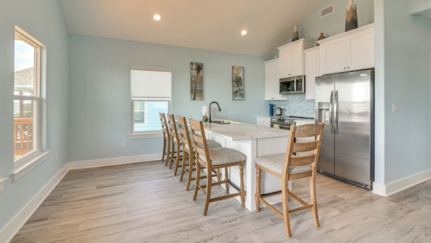A kitchen with a central island, wooden chairs, white cabinets, stainless steel appliances, and artwork on the walls. - Port Bolivar Beach House w/ Oceanfront Views! (Port Bolivar)