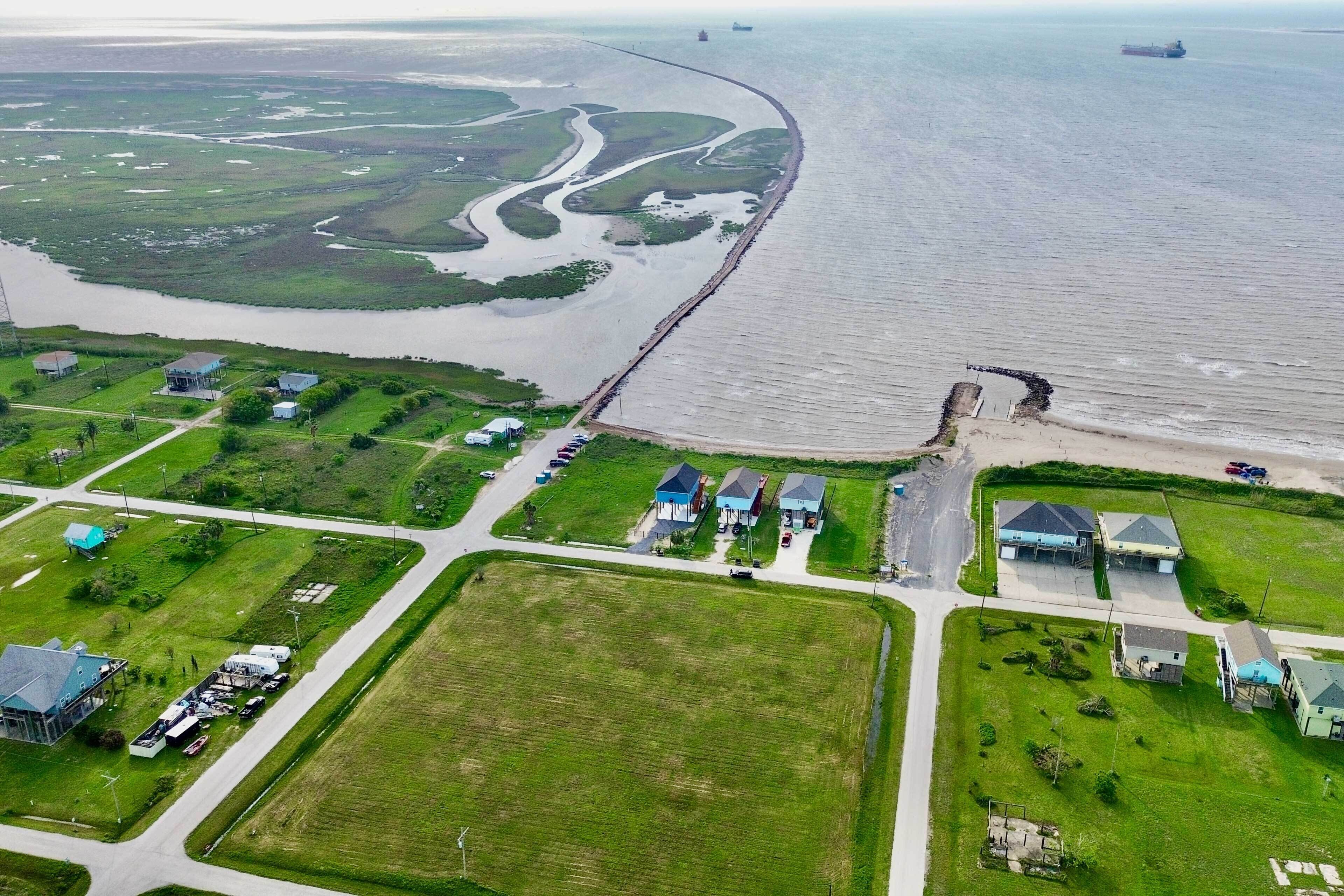 Eine Luftaufnahme einer Küstenregion mit einer langen Pier, die sich ins Wasser erstreckt, umgeben von grünen Feldern und Wohngebäuden.