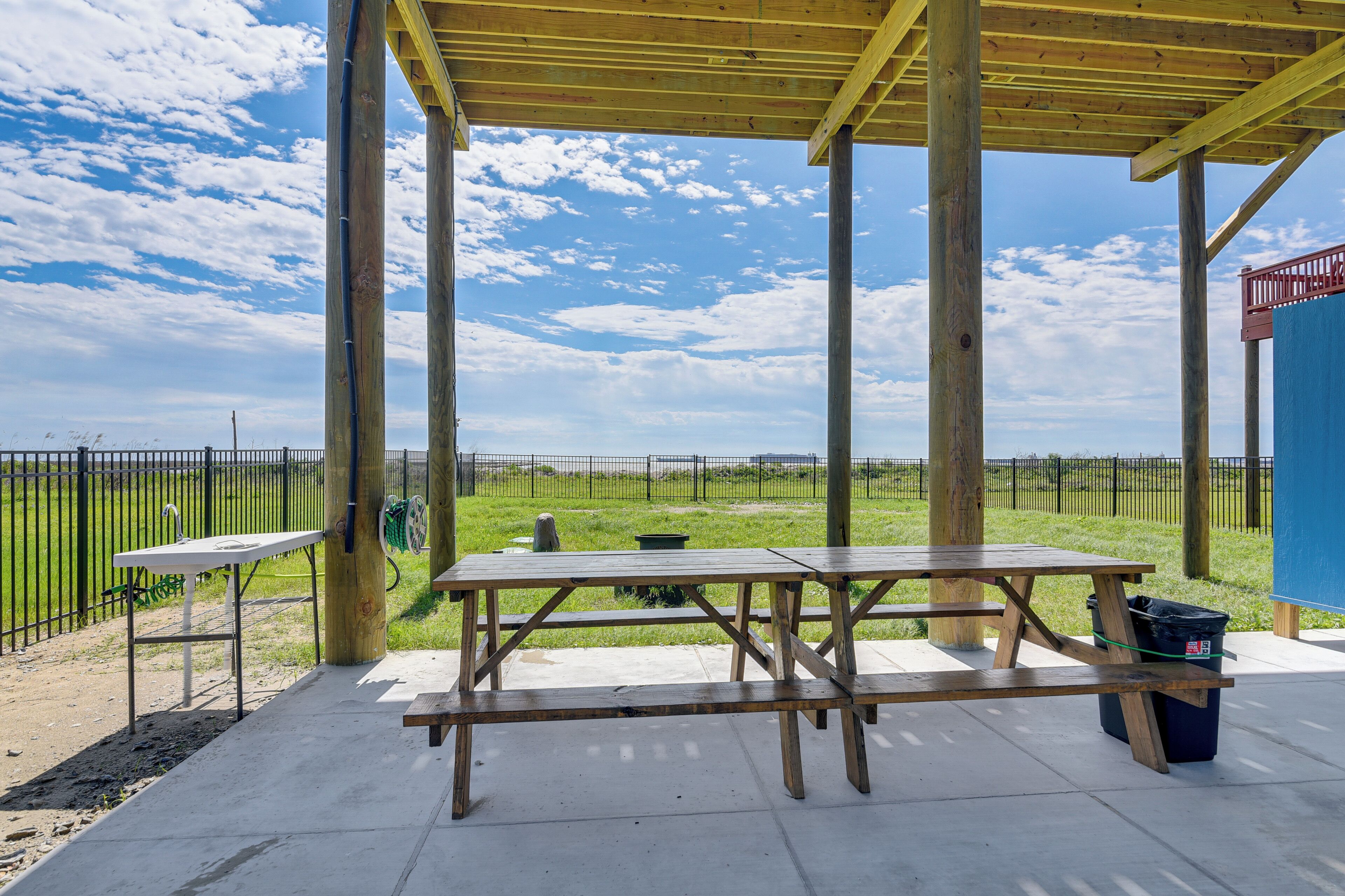 Un espace extérieur aménagé avec une table de pique-nique en bois, offrant une vue sur la plage et donnant sur un terrain clos.