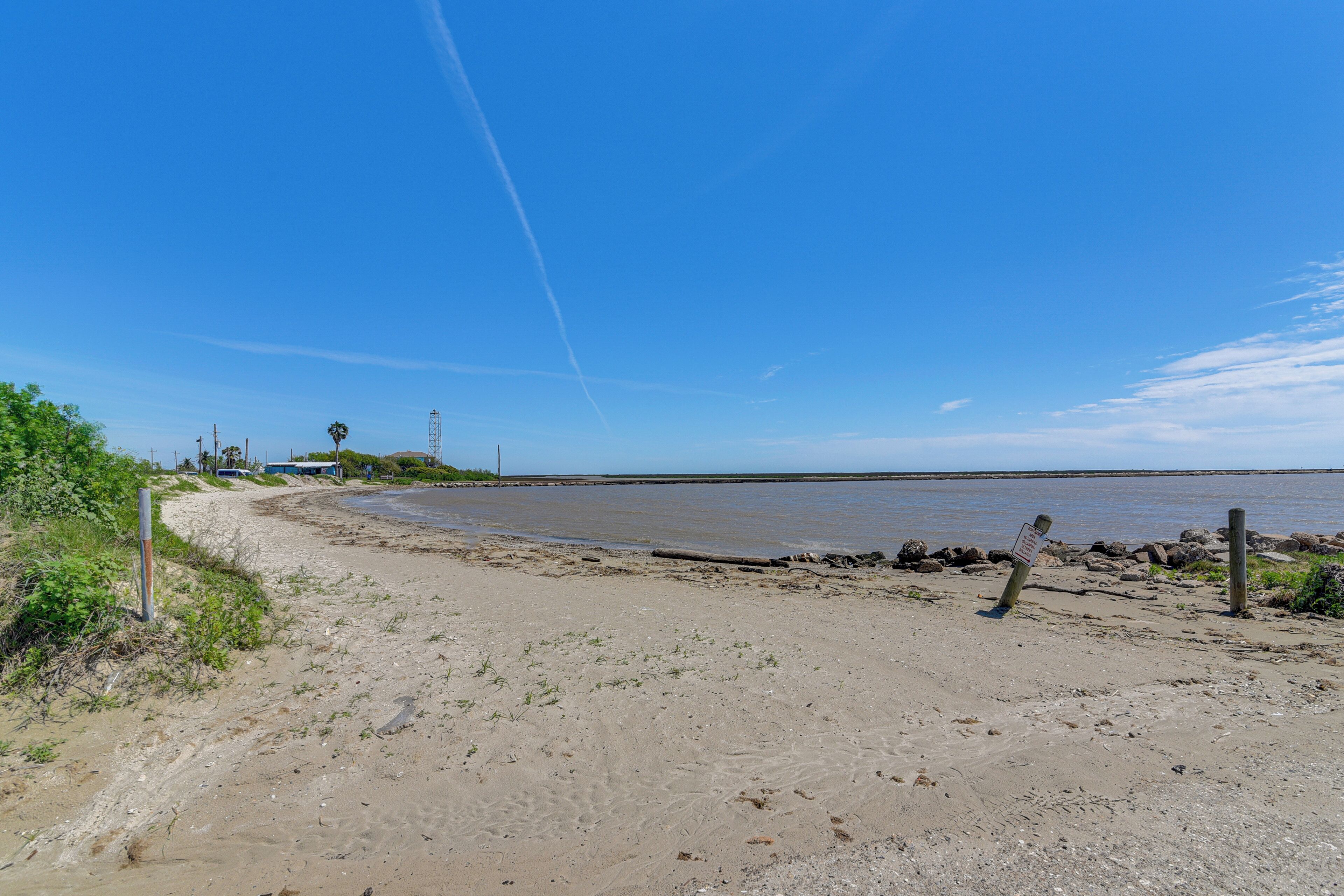 Een zandstrand met een helderblauwe lucht, een houten omheining en een rustig wateroppervlak.