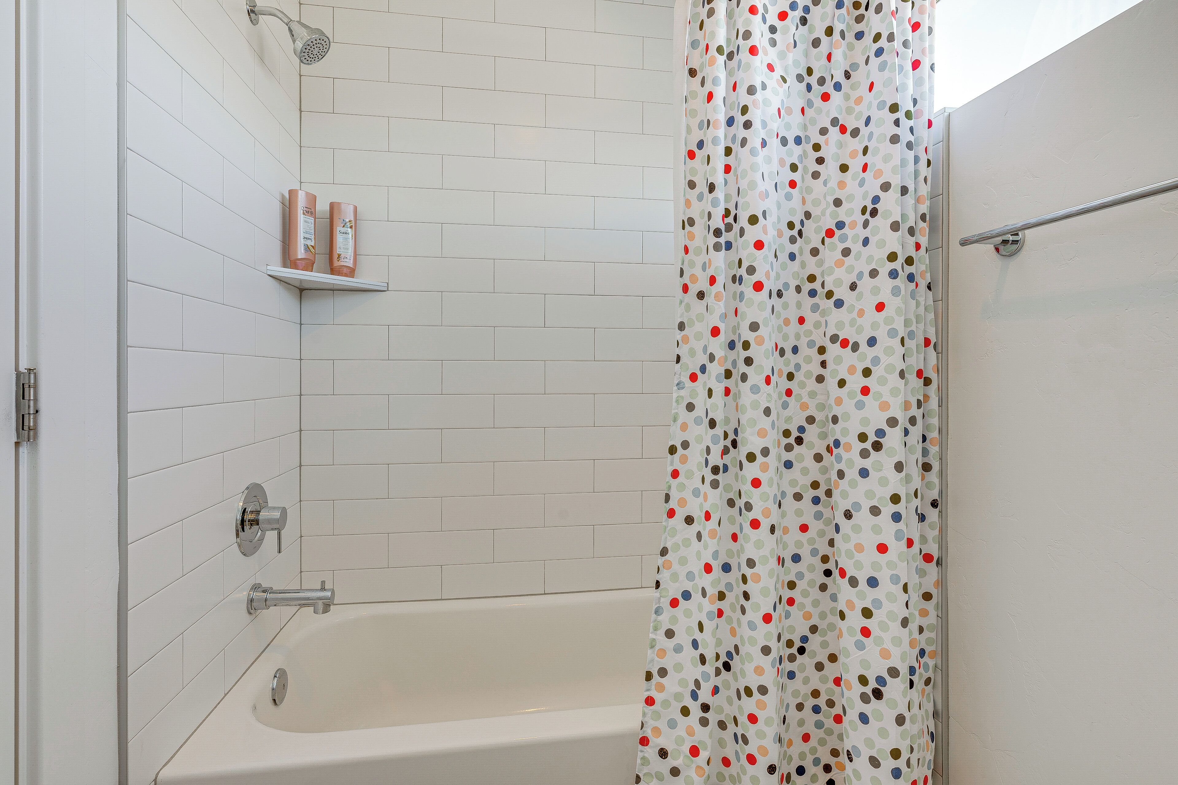 Une salle de bain avec une baignoire blanche, une pomme de douche et un rideau de douche à pois.