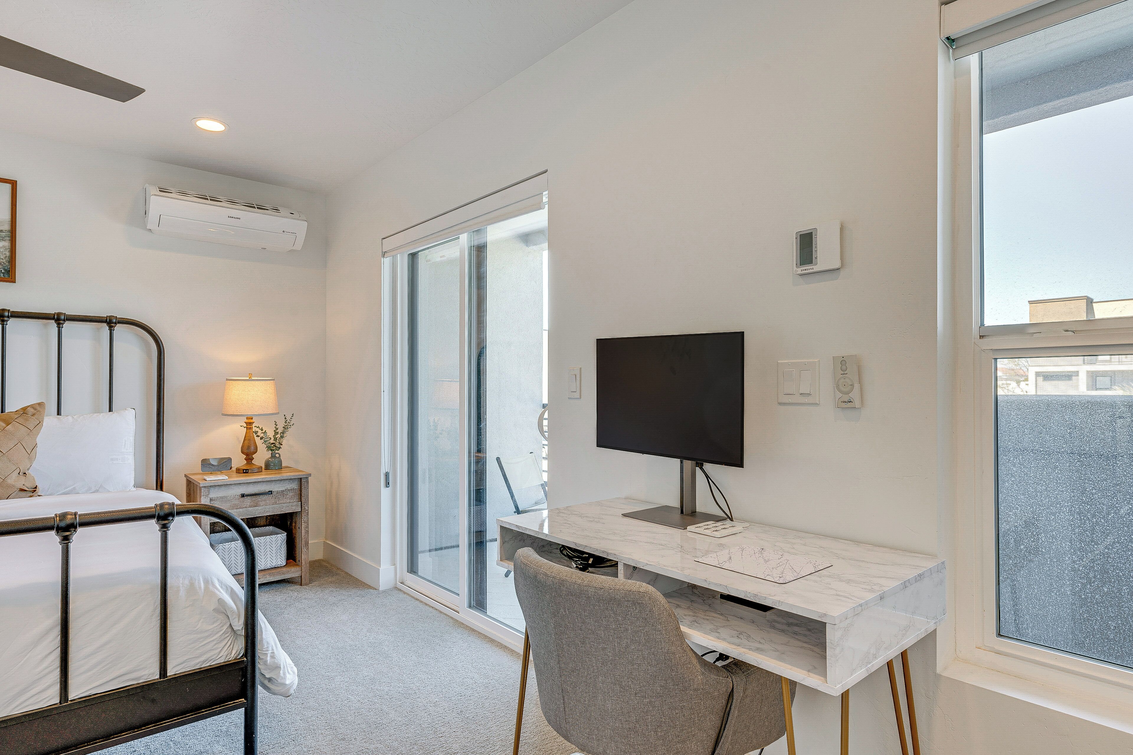 A hotel room with a bed, desk, chair, TV, and large windows.