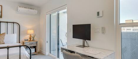 A hotel room with a bed, desk, chair, TV, and large windows.