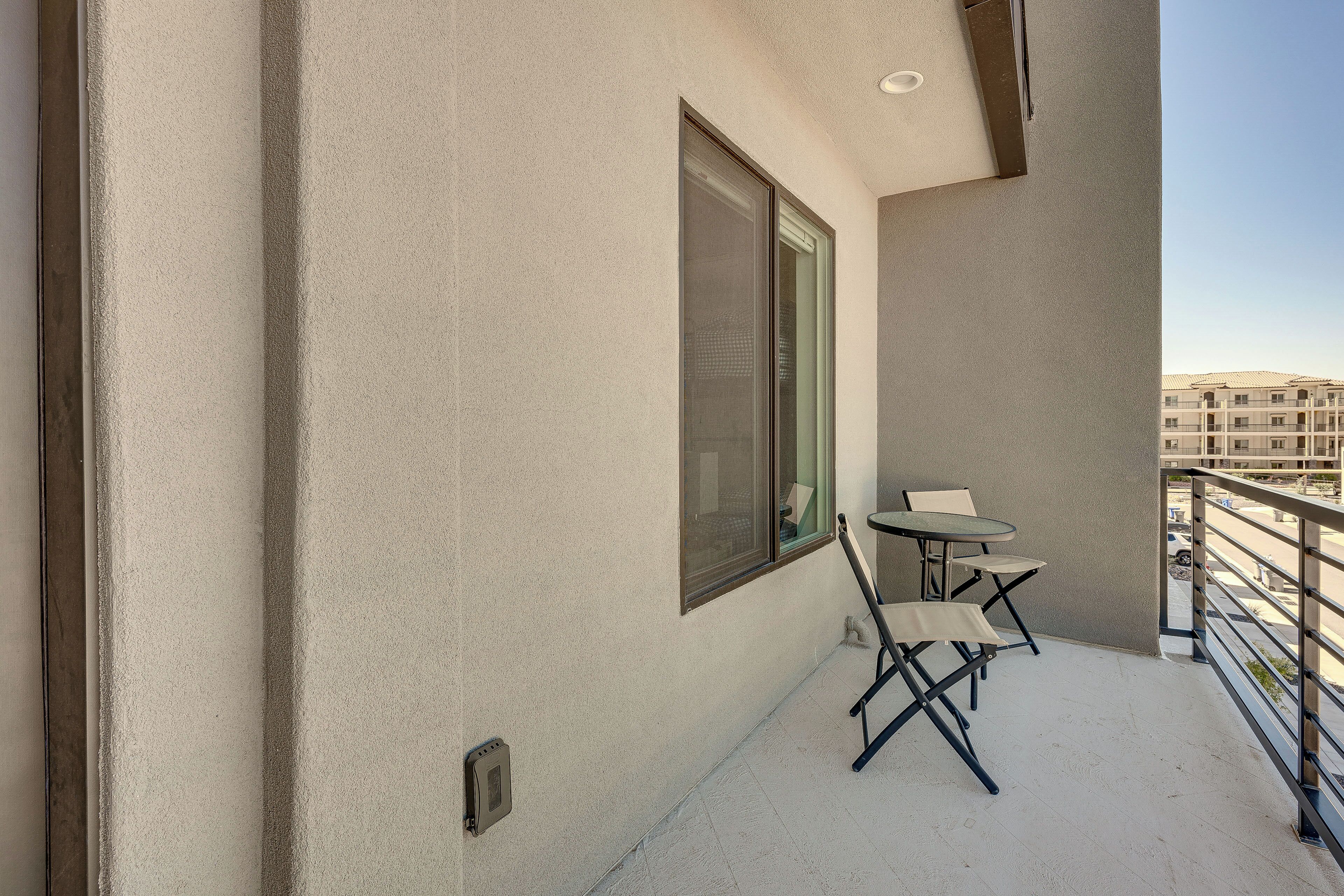 A balcony with a small table and chairs, a window, and a view of a building across the street.