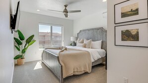 A bedroom with a bed, a ceiling fan, a large window, and a potted plant. - St George Home w/ Patio - 8 Mi to Snow Canyon! (St. George)