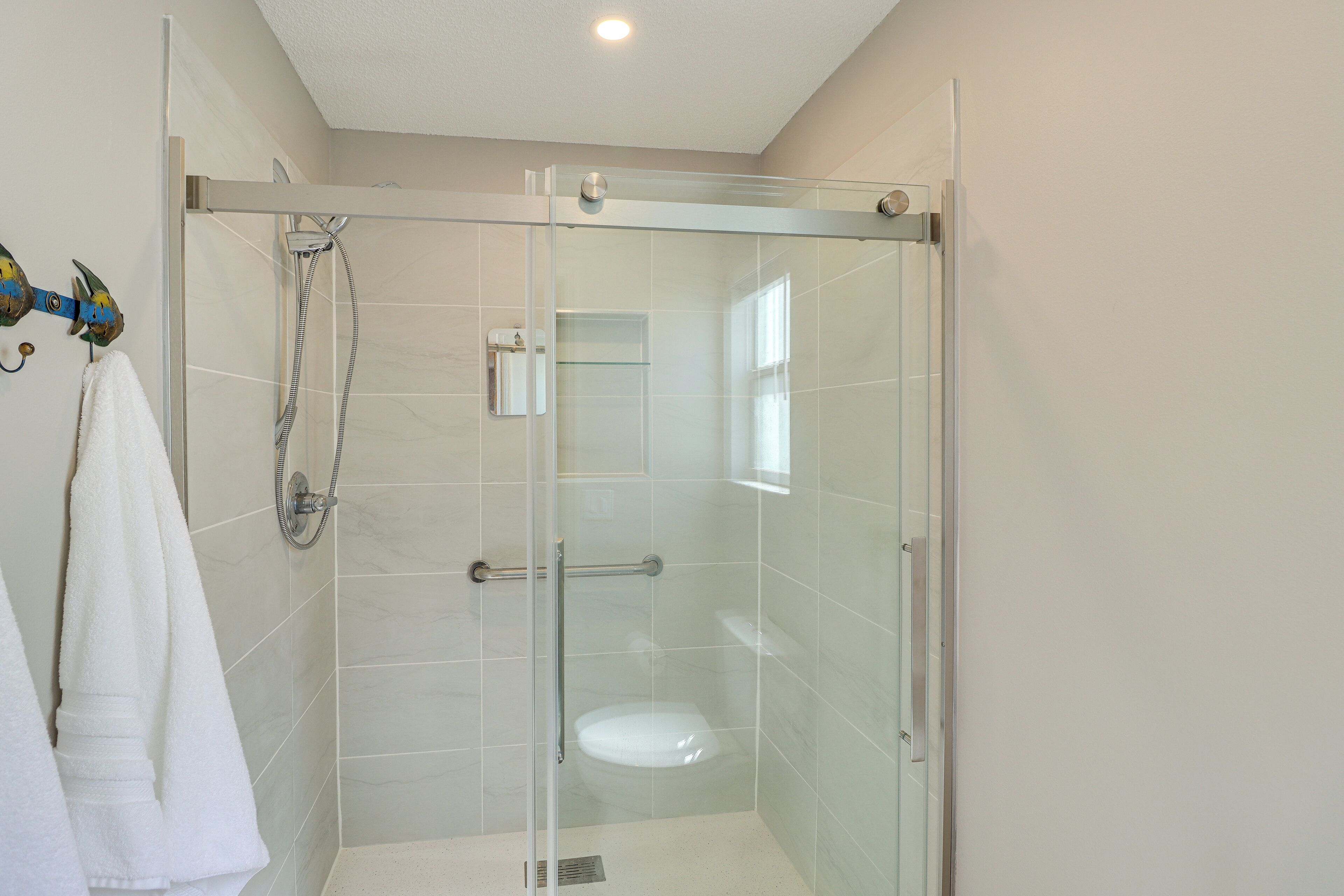 A glass-enclosed shower stall with a glass door, a white toilet, and a towel rack with a white towel.