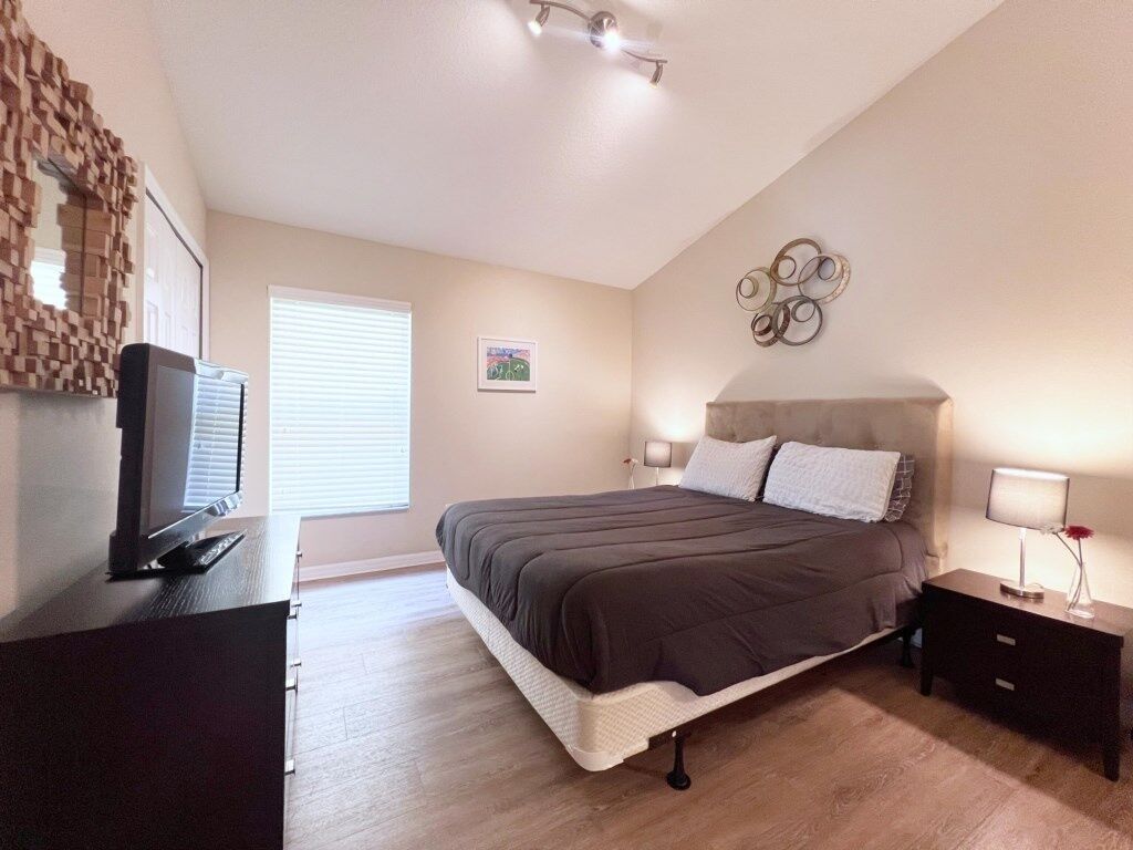 Een slaapkamer met een bed, nachtkastjes, een televisie en een raam met zonwering.