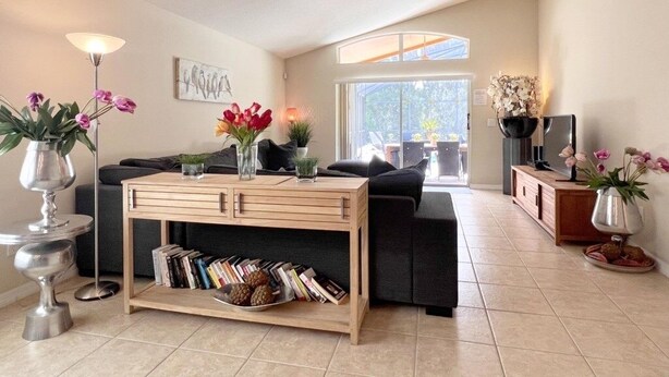 A modern living room with a sofa, coffee table, and decorative plants. - Great Privacy By Pool- Pool Home With Game Room 4 Bedroom Home by RedAwning (Davenport)
