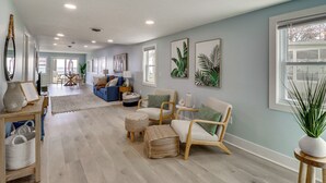 A spacious living room with a light blue wall, wooden flooring, and a large window. There are two sofas, a coffee table, and a side table with a vase. - Bayfront Maryland Retreat w/ Deck, Near Beaches! (North Beach)