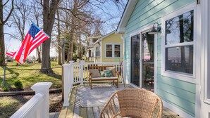 A wooden deck with a wicker chair and a bench, a white fence, and a house with large windows. - Bayfront Maryland Retreat w/ Deck, Near Beaches! (North Beach)