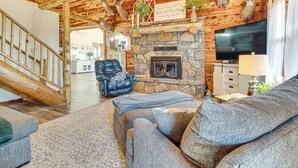A log cabin interior with a stone fireplace, a leather armchair, and a television. - Expansive Mountain Home Rental w/ Yard & Fire Pit! (Mountain Home)