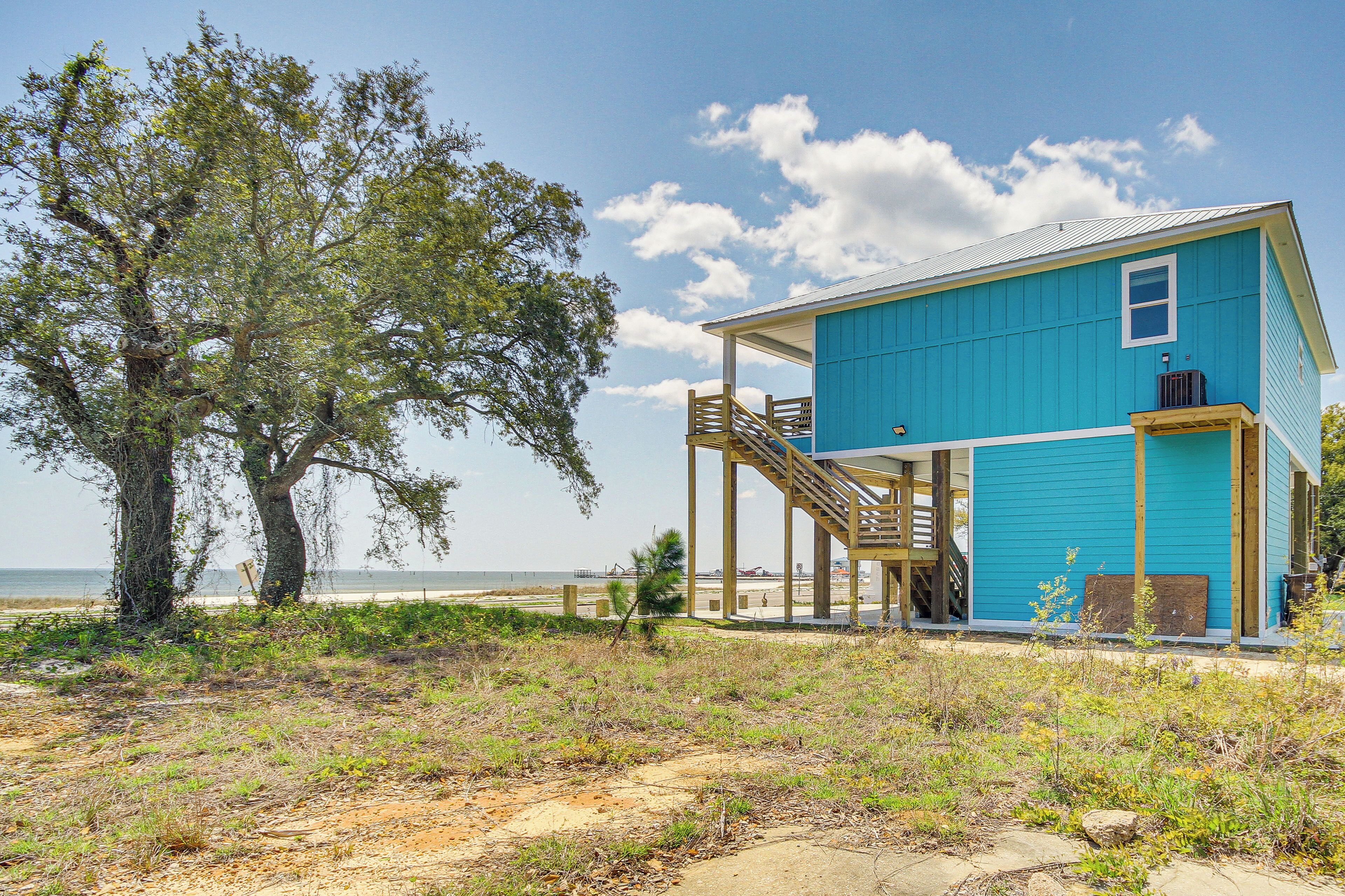 A coastal house with a blue exterior, a wooden staircase, and a view of the beach.